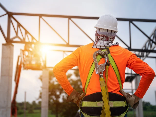A crane operator in orange sweatshirt standing with his back to us.